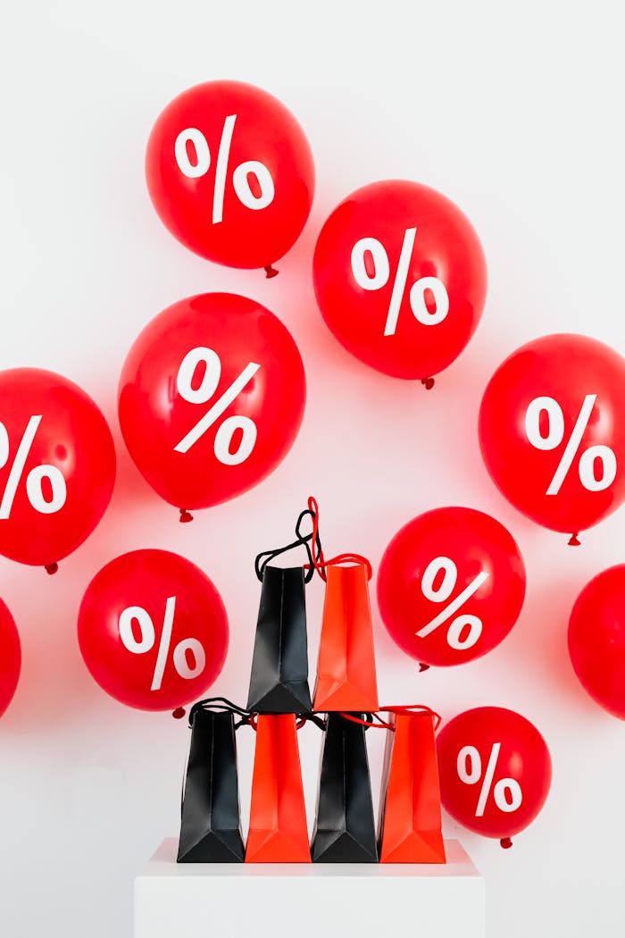 Vibrant red balloons with percentage signs and shopping bags for sales event.