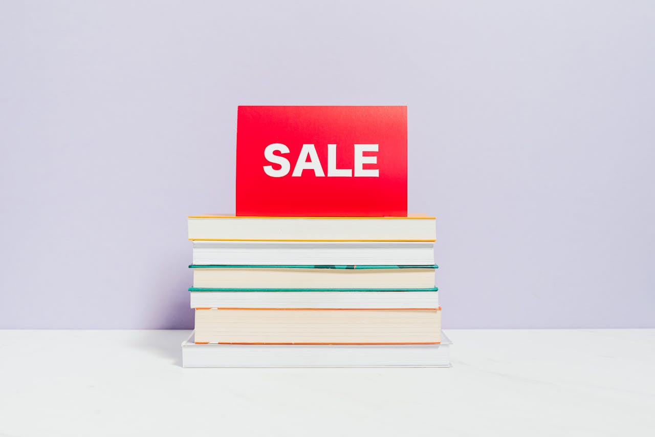 A stack of books with a red sale sign, ideal for promotions and bookshop advertisements.